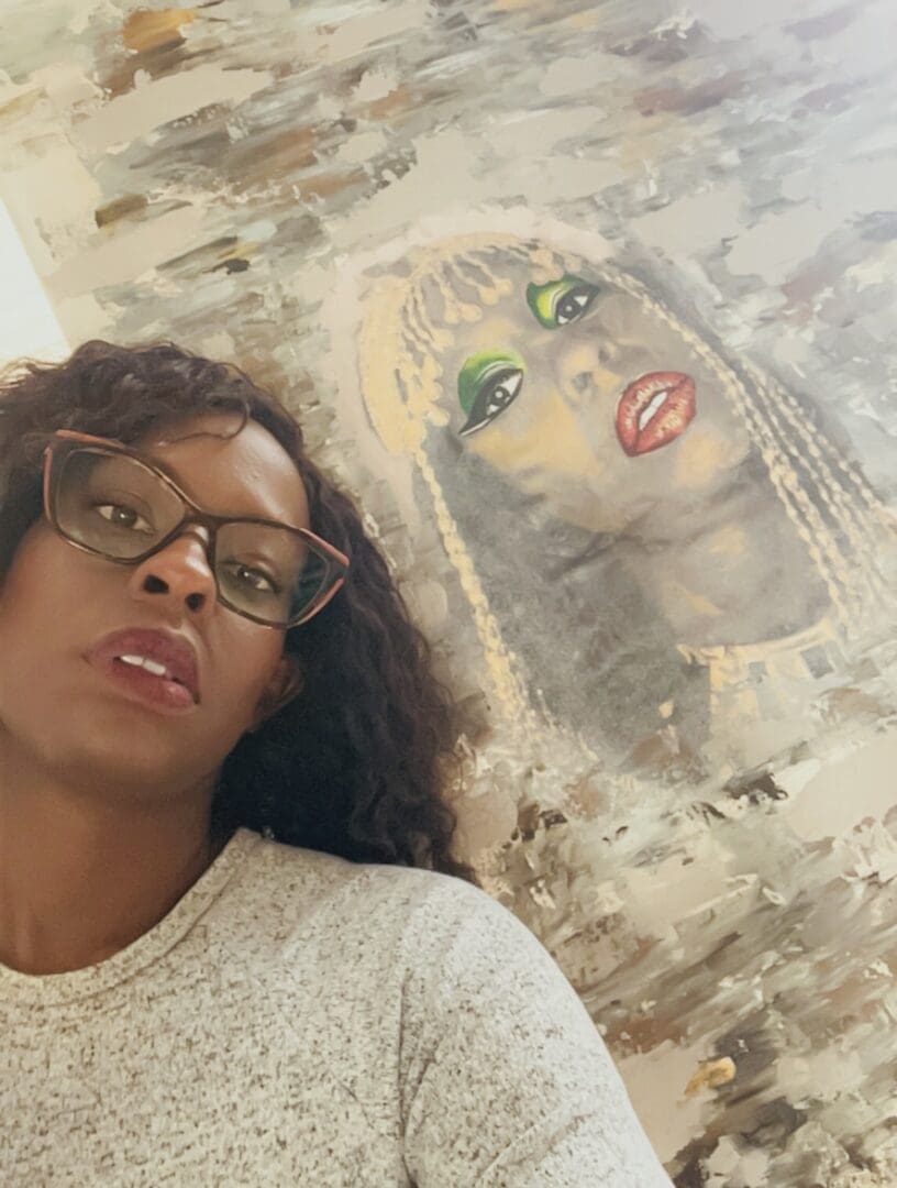 A woman with glasses and a white shirt is in front of a picture.
